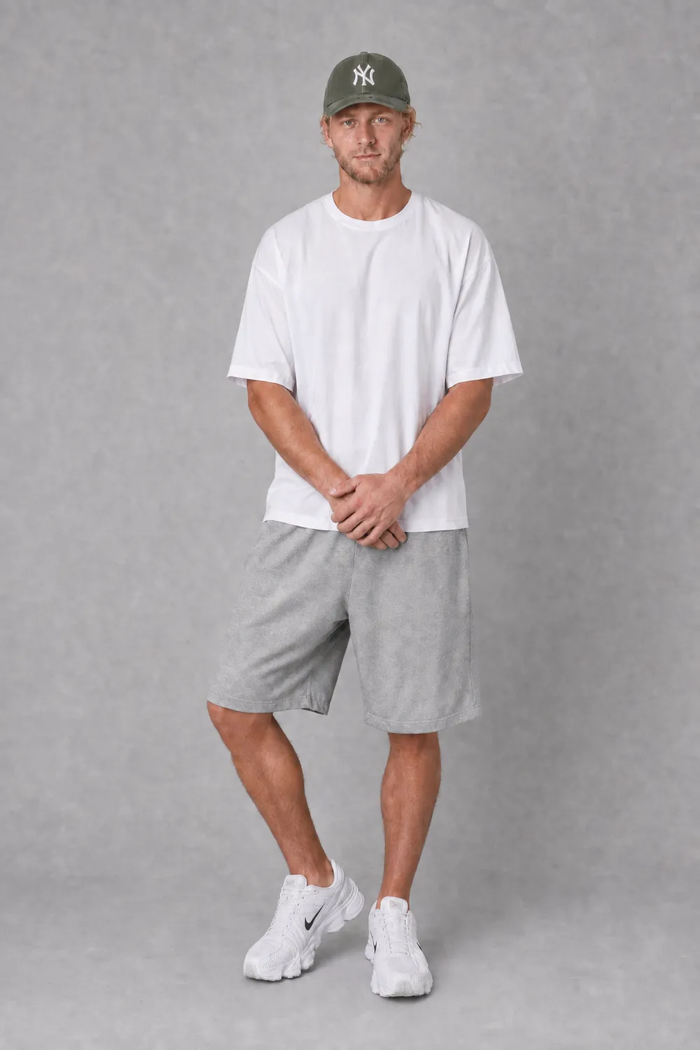 KI-generiertes On-Model-Bild: Model in weissem Oversize-Shirt, Cap und grauen Shorts